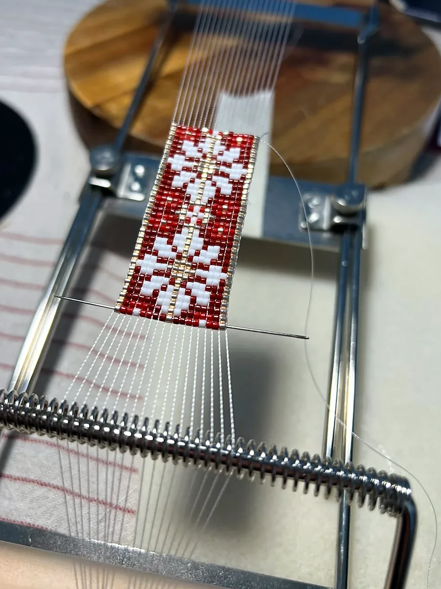 Pulsera Carmesí recién empezada en el telar, con la aguja pasada entre los hilos