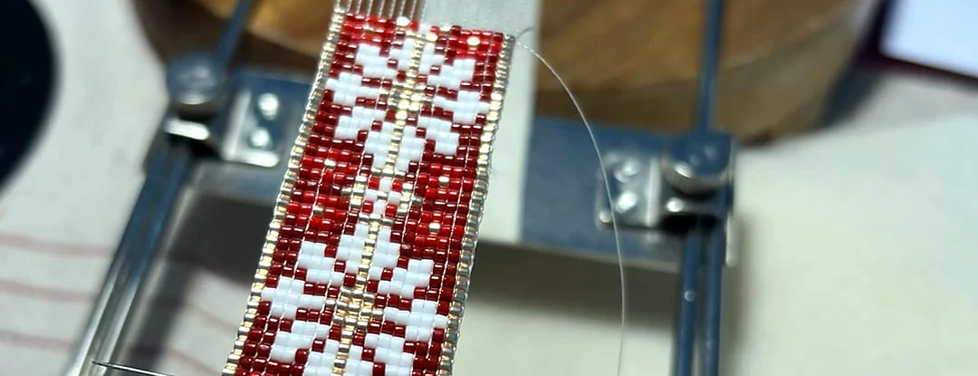 Pulsera Carmesí a medio tejer en el telar, con la aguja y los hilos